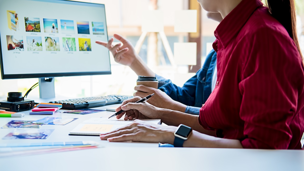 A Woman in a Red Shirt Works for Global Campaigns While Referencing Images on a Large Computer Screen in a Bright Office